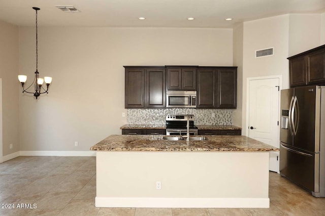 kitchen with sink, stainless steel appliances, pendant lighting, stone countertops, and a center island with sink