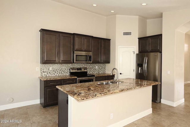 kitchen with light stone counters, sink, stainless steel appliances, and an island with sink