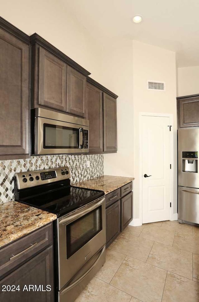 kitchen with tasteful backsplash, light stone counters, dark brown cabinets, and stainless steel appliances