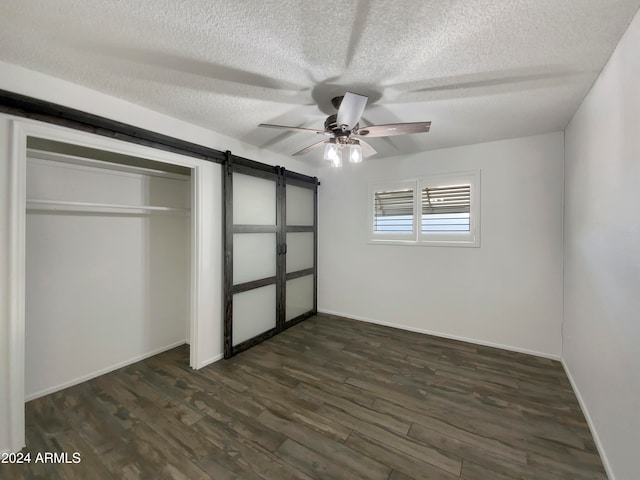 unfurnished bedroom with ceiling fan, dark hardwood / wood-style flooring, a textured ceiling, a barn door, and a closet