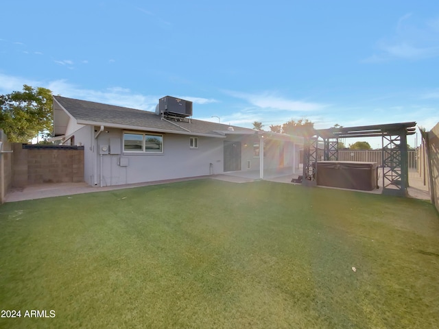 rear view of property featuring a patio, central AC, a hot tub, and a lawn