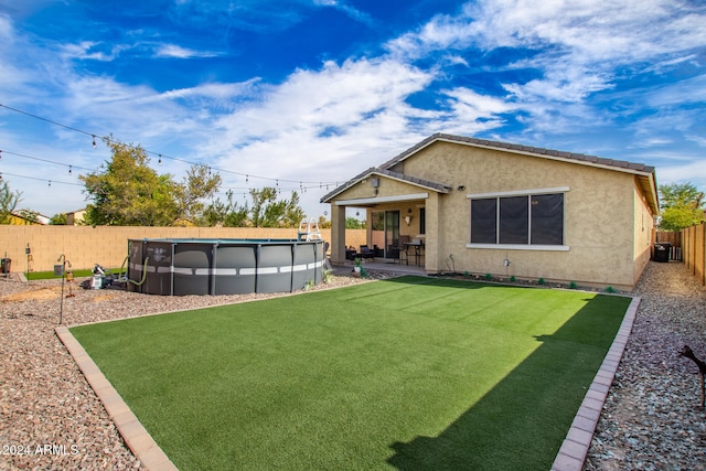 back of property with central AC unit, a patio area, a lawn, and a fenced in pool