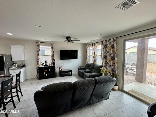 living room featuring visible vents, light tile patterned flooring, ceiling fan, a textured ceiling, and baseboards