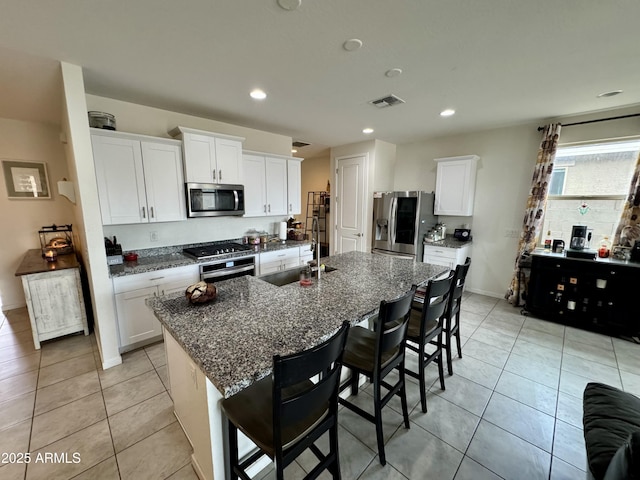 kitchen with stainless steel appliances, a kitchen island with sink, light tile patterned flooring, a sink, and a kitchen bar