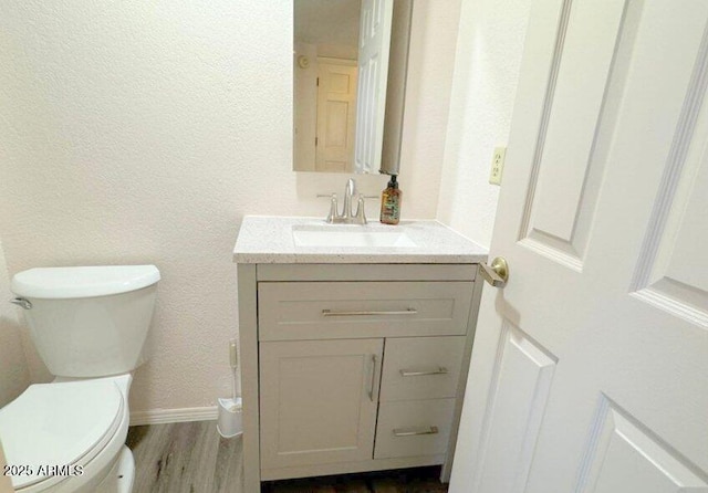 bathroom featuring a textured wall, toilet, vanity, wood finished floors, and baseboards