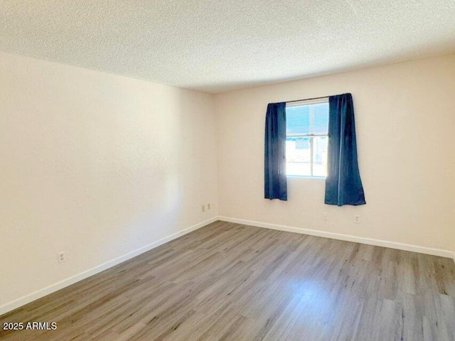 spare room featuring a textured ceiling, baseboards, and wood finished floors