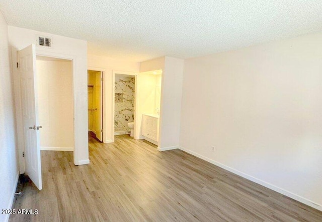 unfurnished bedroom with baseboards, visible vents, ensuite bath, a textured ceiling, and light wood-style floors