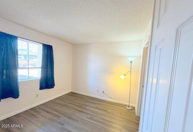 unfurnished bedroom featuring a textured ceiling, baseboards, and wood finished floors