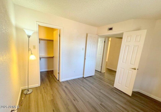 unfurnished bedroom with a closet, a spacious closet, a textured ceiling, wood finished floors, and baseboards