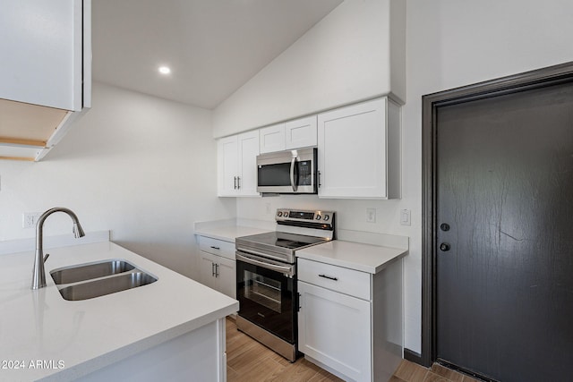 kitchen with appliances with stainless steel finishes, vaulted ceiling, sink, light hardwood / wood-style floors, and white cabinetry