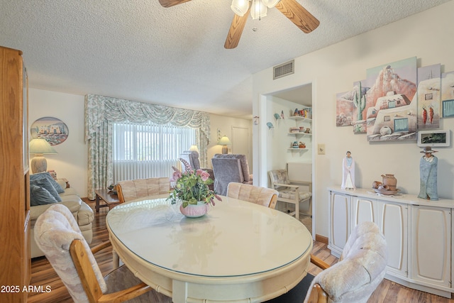 dining space with light wood-style flooring, visible vents, ceiling fan, and a textured ceiling