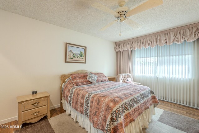 bedroom with a textured ceiling, ceiling fan, light wood-type flooring, and baseboards