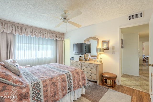 bedroom featuring a ceiling fan, a textured ceiling, visible vents, and wood finished floors