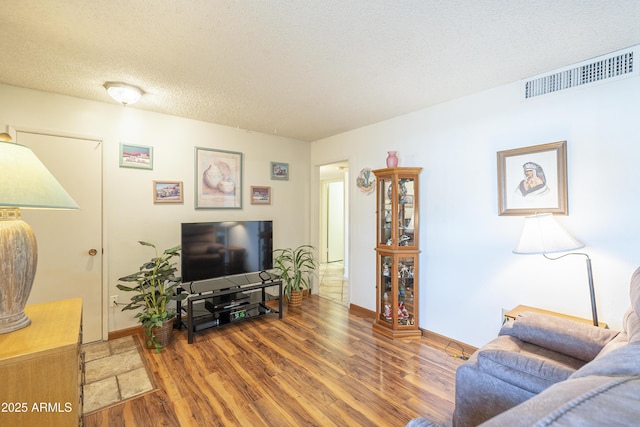 living room featuring baseboards, a textured ceiling, visible vents, and wood finished floors