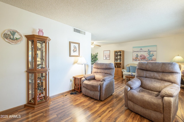 living room with a textured ceiling, wood finished floors, visible vents, and baseboards