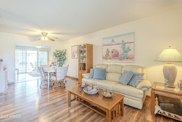 living area with a textured ceiling, wood finished floors, a ceiling fan, and baseboards