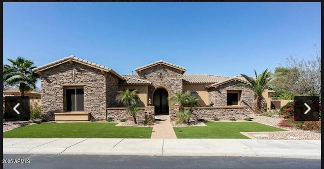 mediterranean / spanish home with stone siding, a tile roof, a front yard, and stucco siding