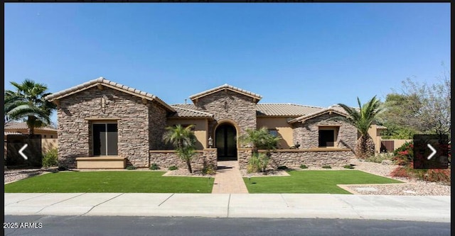 mediterranean / spanish home with fence, a tiled roof, stone siding, stucco siding, and a front lawn