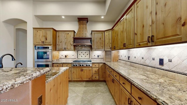 kitchen featuring tasteful backsplash, appliances with stainless steel finishes, light stone countertops, and custom range hood