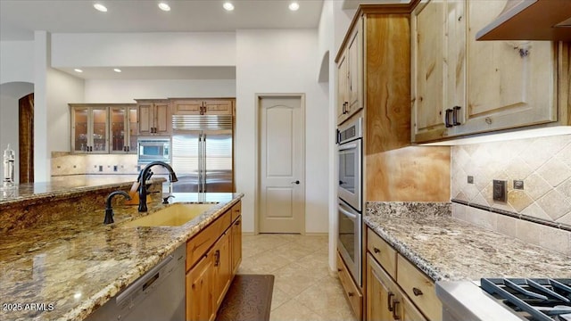 kitchen with range hood, tasteful backsplash, sink, built in appliances, and light stone counters