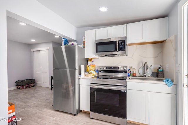 kitchen featuring decorative backsplash, white cabinetry, sink, light hardwood / wood-style floors, and stainless steel appliances