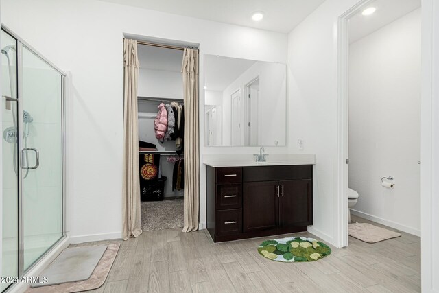 bathroom with toilet, a shower with door, hardwood / wood-style flooring, and vanity