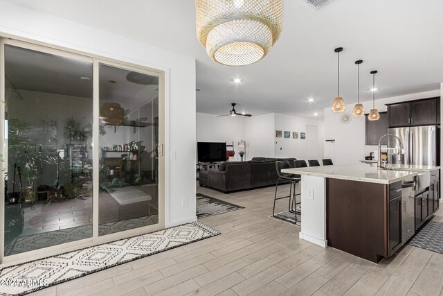 kitchen with ceiling fan with notable chandelier, a center island with sink, light hardwood / wood-style floors, sink, and light stone counters