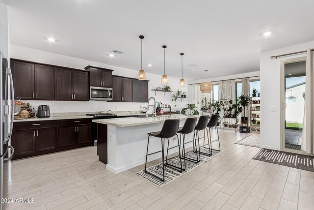 kitchen with decorative light fixtures, light stone counters, stainless steel appliances, an island with sink, and a breakfast bar area