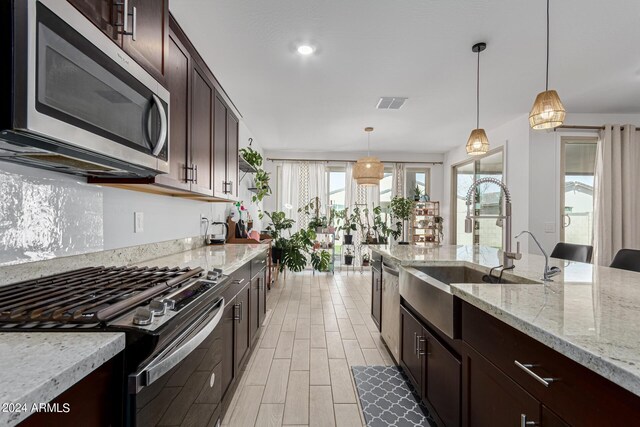 kitchen with hanging light fixtures, light hardwood / wood-style flooring, light stone countertops, stainless steel appliances, and sink