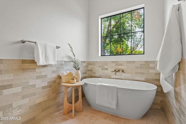 full bath with tile walls, wainscoting, tile patterned flooring, and a freestanding bath
