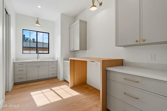 kitchen with gray cabinetry, light countertops, light wood finished floors, and a sink