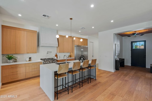 kitchen with a kitchen breakfast bar, visible vents, stainless steel built in fridge, a center island with sink, and a sink