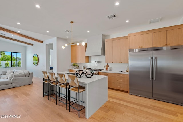 kitchen featuring visible vents, a kitchen breakfast bar, wall chimney range hood, light countertops, and appliances with stainless steel finishes
