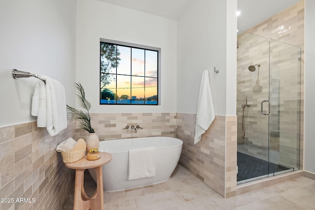 full bathroom featuring tile patterned floors, a wainscoted wall, a freestanding tub, tile walls, and a stall shower
