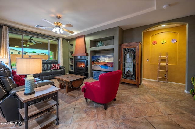 tiled living room featuring a raised ceiling, built in features, and ceiling fan