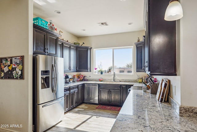 kitchen with sink, appliances with stainless steel finishes, hanging light fixtures, dark brown cabinetry, and light stone countertops