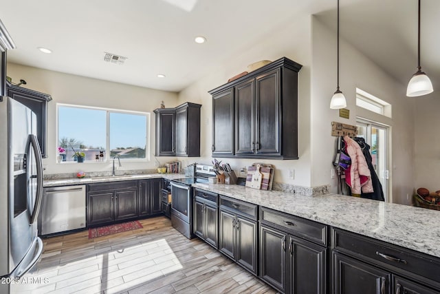 kitchen with light stone countertops, appliances with stainless steel finishes, sink, and decorative light fixtures