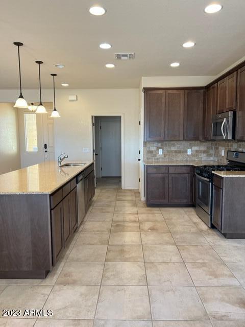 kitchen featuring sink, light stone countertops, decorative light fixtures, dark brown cabinetry, and stainless steel appliances