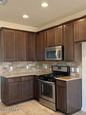 kitchen featuring decorative backsplash, dark brown cabinets, light tile patterned flooring, and appliances with stainless steel finishes