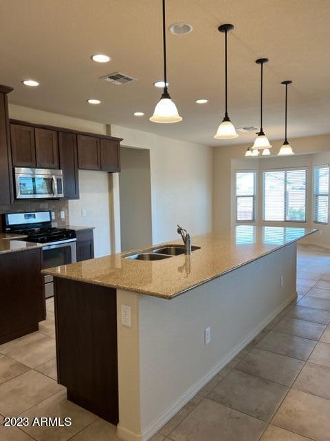 kitchen featuring sink, hanging light fixtures, light stone counters, a kitchen island with sink, and appliances with stainless steel finishes