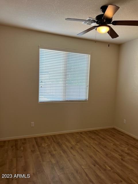 empty room with ceiling fan, wood-type flooring, and a textured ceiling