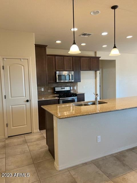 kitchen featuring light stone counters, sink, hanging light fixtures, and appliances with stainless steel finishes