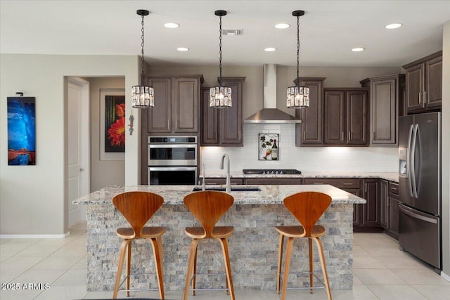 kitchen with tasteful backsplash, wall chimney range hood, a center island with sink, and appliances with stainless steel finishes