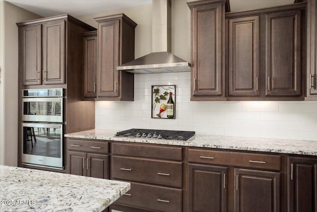 kitchen with appliances with stainless steel finishes, wall chimney exhaust hood, dark brown cabinetry, and backsplash