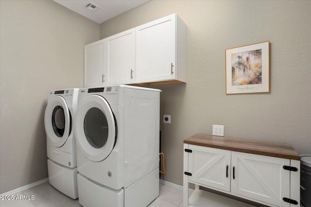 clothes washing area with cabinets, washer and clothes dryer, and light tile patterned floors