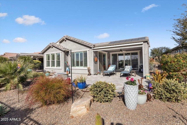 back of property with ceiling fan, a patio, and solar panels