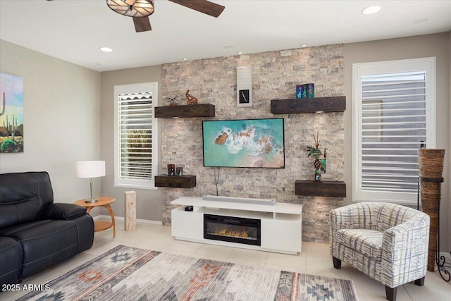 tiled living room with ceiling fan and a fireplace