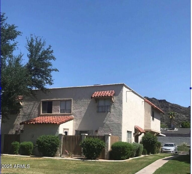 view of property exterior featuring a tile roof, fence, a yard, a mountain view, and stucco siding