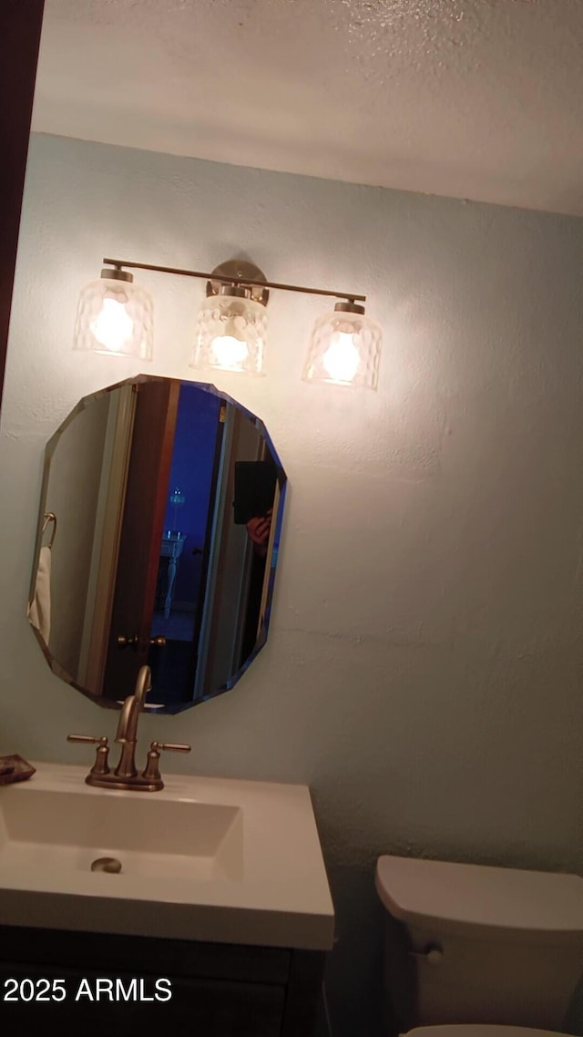 half bathroom with a textured ceiling, vanity, and toilet