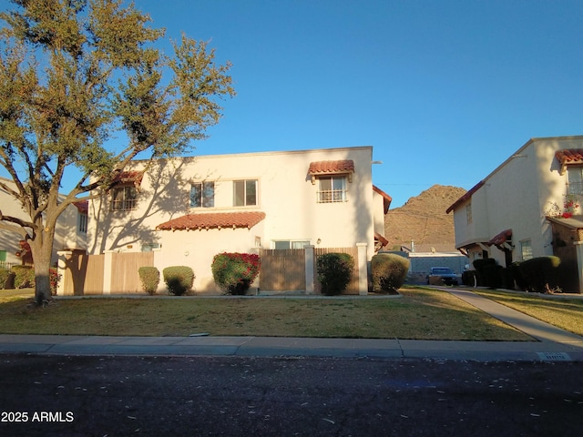 view of front facade with a tile roof, fence, a front lawn, and stucco siding